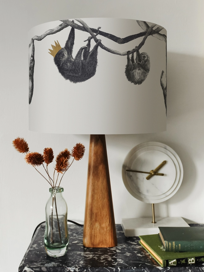 Drum Lampshade featuring Sloths on a wooden base on a shelf with books and ornaments