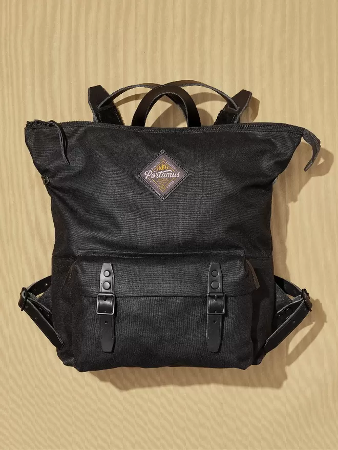 Black wax cotton zip top Shortwood backpack with black leather trim and hardware on a taupe background.