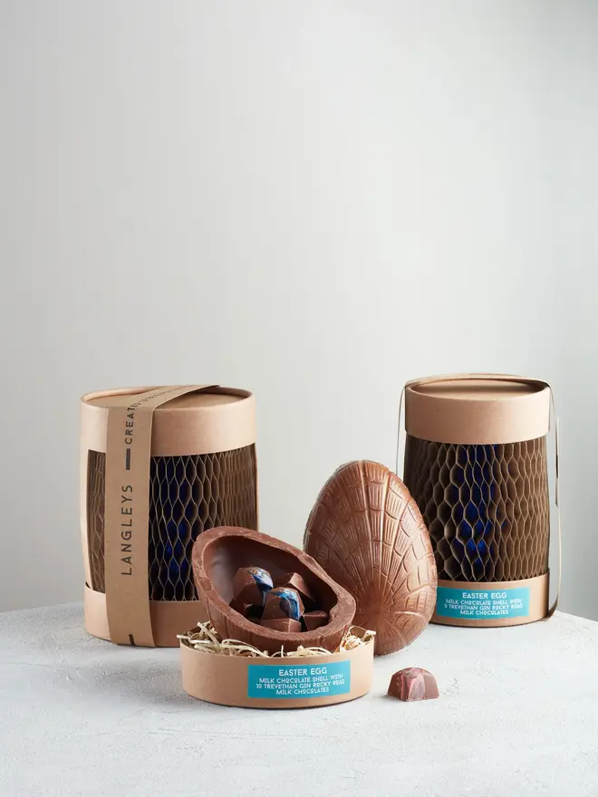 Extra Thick Milk Chocolate Easter Egg With Trevethan Gin, a chocolate egg sitting on a white surface. It is accompanied by another chocolate egg that is opened showing the chocolates within. 