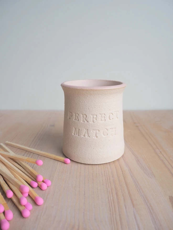 Stoneware match pot saying 'perfect match', pale pink inside with pink tip matches lay to the side of the pot