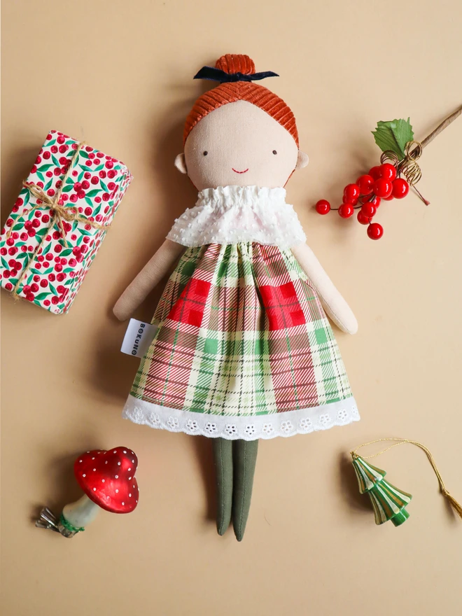 Handmade cloth doll with red brown corduroy hair in a top knot tied with a navy velvet bow, wearing a white textured ruffle collar, a red and green tartan dress with lace trim, and dark green tights.