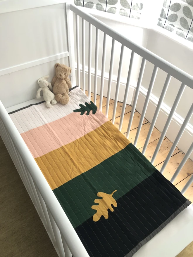 Autumn Leaf Stripe Cotton Baby Quilt/ Mat. A multicoloured stripe quilt with leaf motif shown in a nursery.