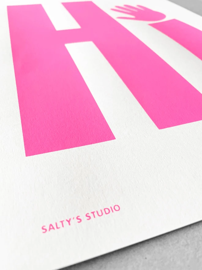 Close up of a neon pink printed Hi upon a white sheet on paper - sat on a grey background. Cose up shows the Salty's Studio printed in the bottom left corner
