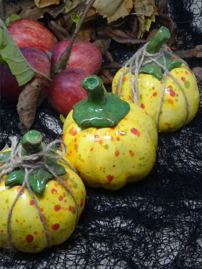 A ceramic decorative pumpkin in yellow spotted glaze with a green stem