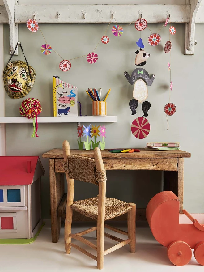 A panda mobile made of multiple parts hanging over a kids desk and next to some vintage toys