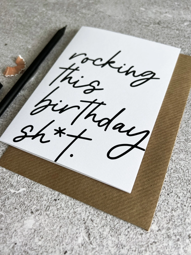 Rocking This Birthday Card laid on a brown envelope next to a black pencil on a stone background.