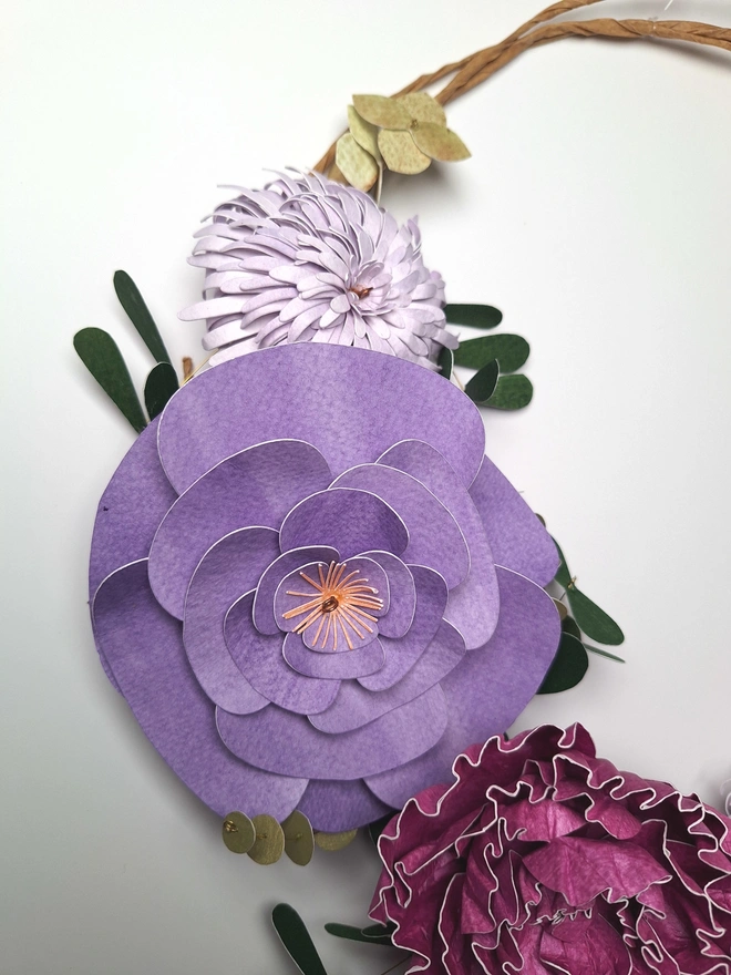 Close up of paper flowers including a pale purple chrysanthemum, a medium purple camelia and a pinkish purple peony.