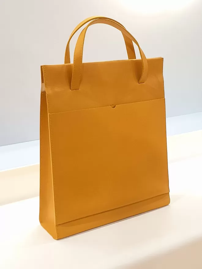 Angled view of the Amber Yellow Tote Bag on a Cream Base Panel shot in yellow lighting