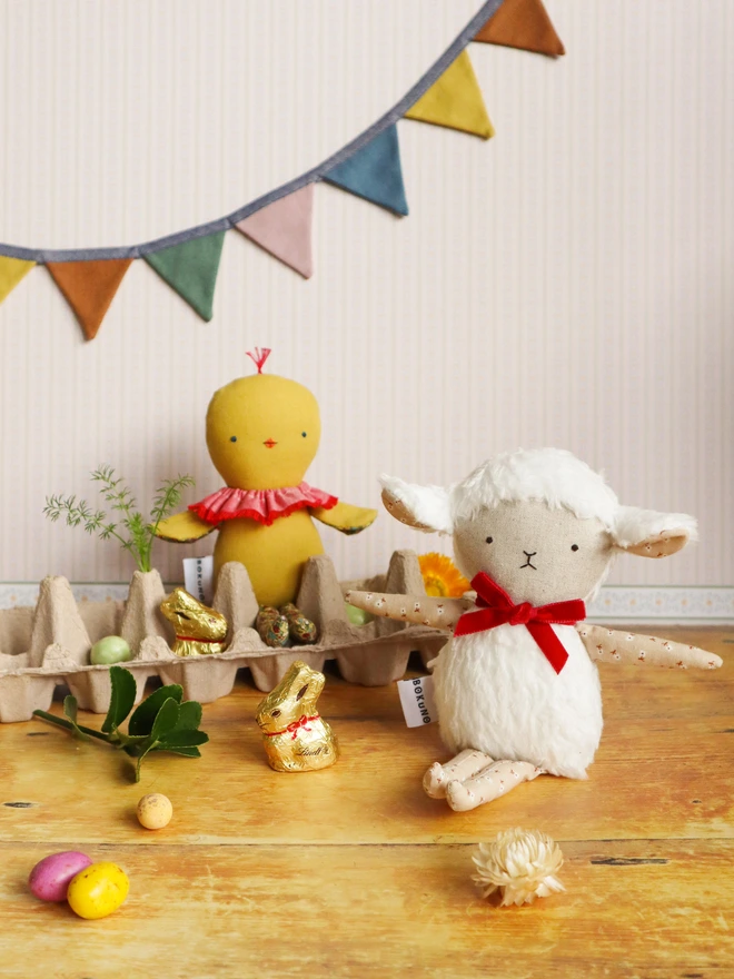 Handmade lamb doll with a fluffy white body, stitched face, beige floral fabric arms and legs, and a small red velvet bow tied around its neck.