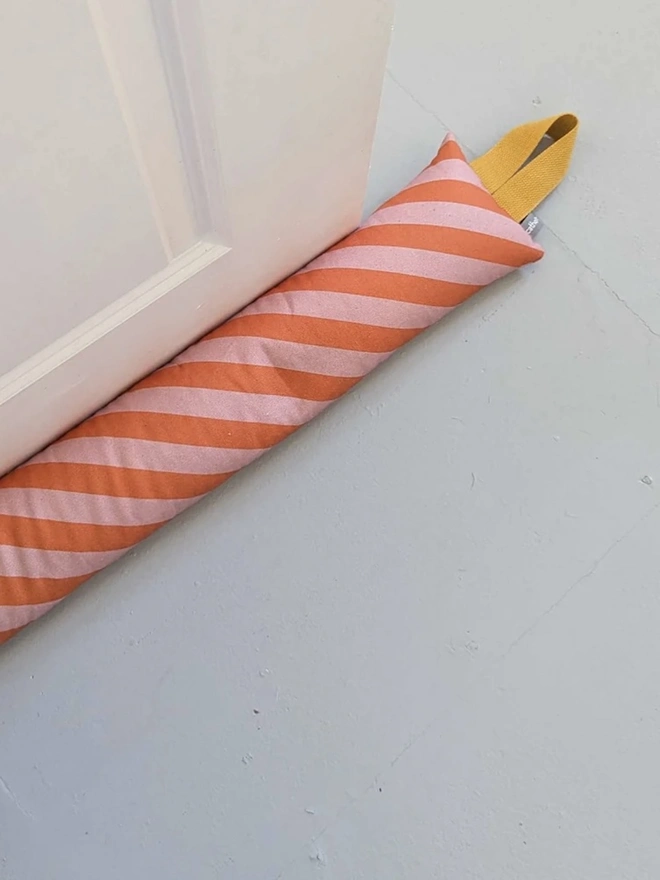 Draught Excluder, a colourful patterned draught excluder sitting on the floor by a white door. 