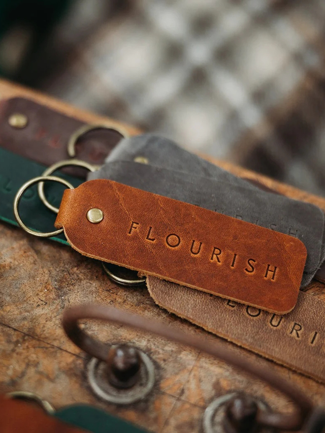  encouraging leather keyring. a brown keyring in the foreground embossed with the word 'flourish'.