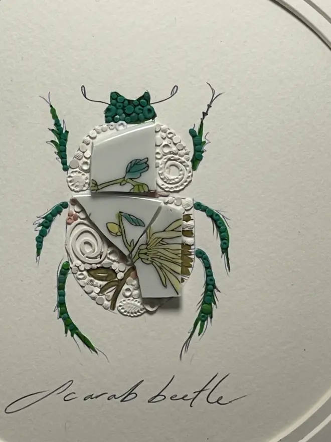 Hand-drawn, painted, mosaic clay, vintage yellow floral pottery insect on white double mounted card, in a black circular frame.