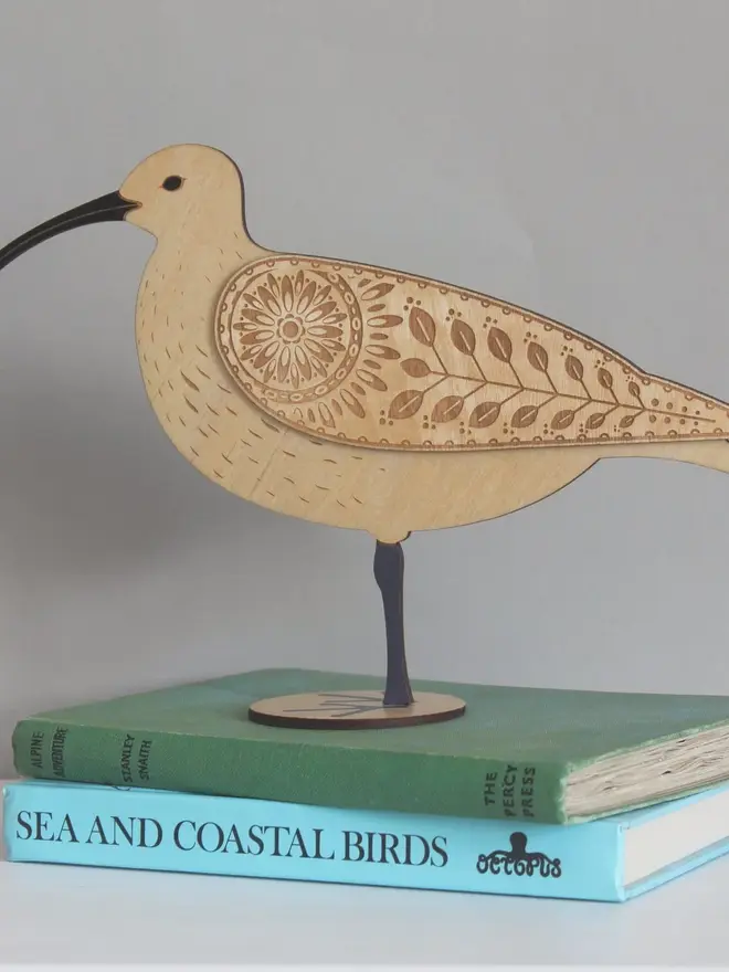 Standing Wooden Curlew, wooden bird decoration standing on a platform on a book. 