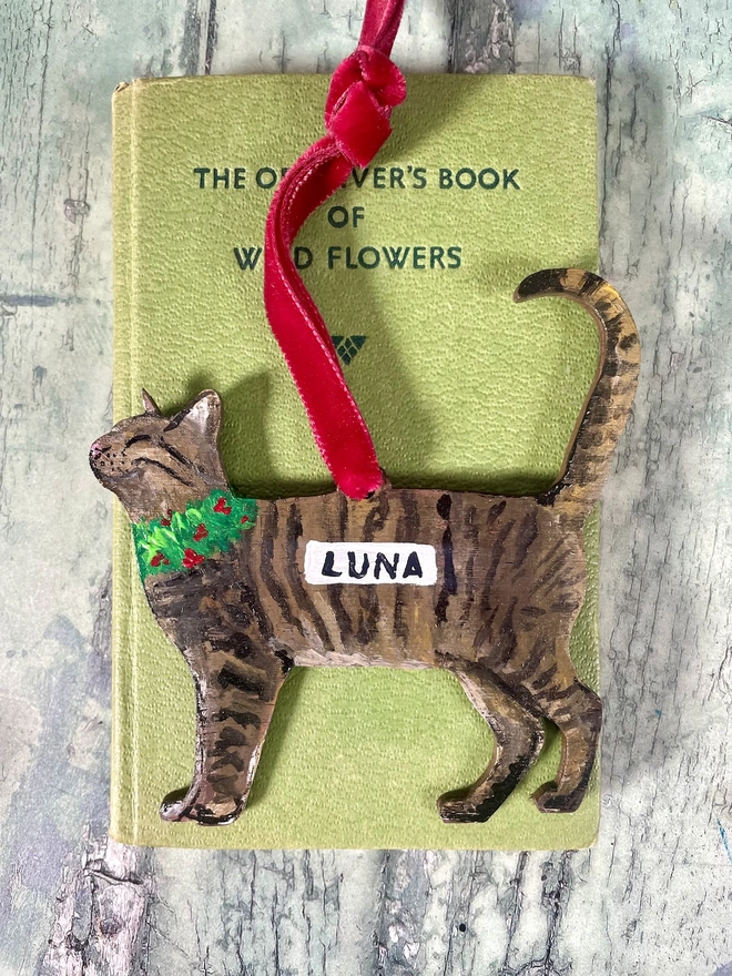 Tabby Cat Christmas Decoration with red velvet ribbon placed onto a book about cats 