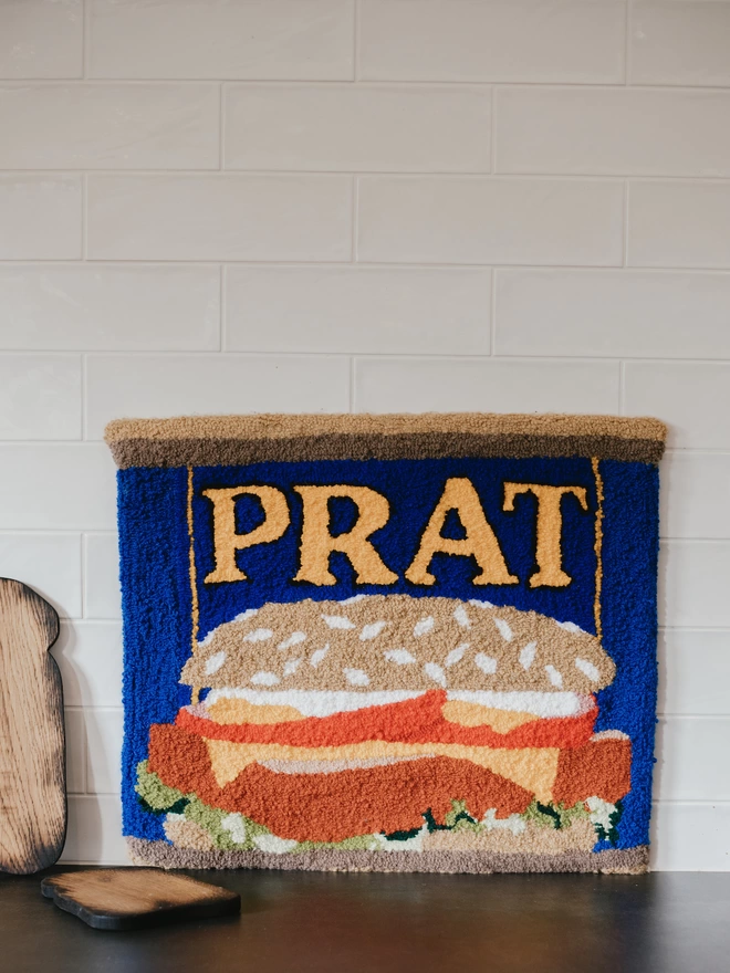 'Prat' Handmade Tufted Rug/Wall Hanging seen up against a kitchen counter with a toast shaped wooden board.