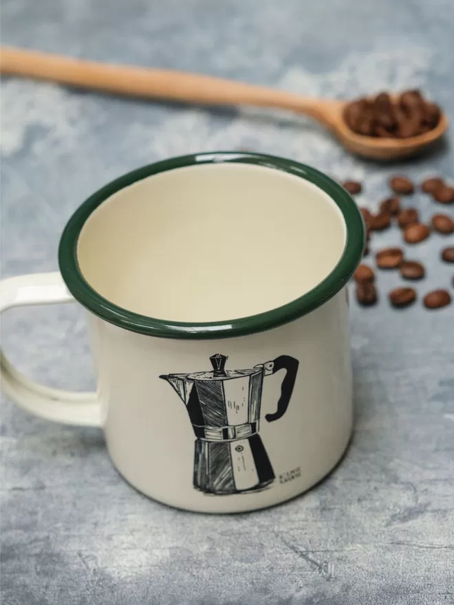 Picture of a Cream Enamel Mug with a Green Rim with a Moka Pot design etched onto it, taken from an original Lino Print