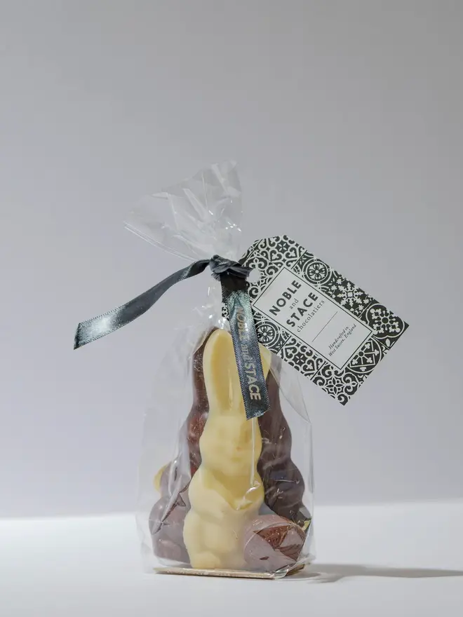Three Easter Bunnies made of milk, white and dark Chocolate tides together in clear plastic against a light background. 