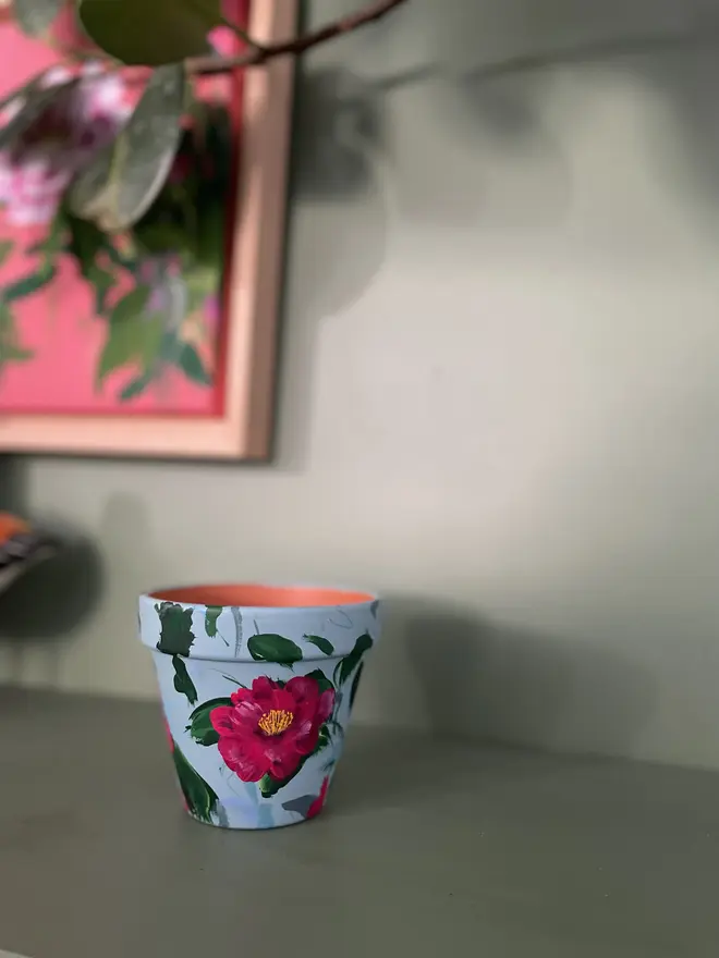 hand painted terrecotta floral plant pot background in a pale blue with rich pink camellia flowers