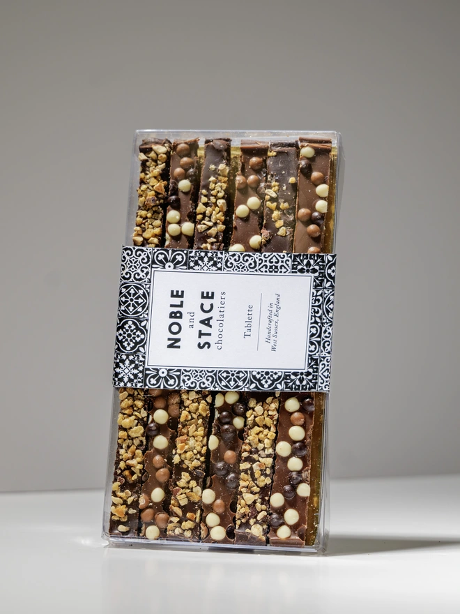 picture of hand cut strips of milk and dark chocolate, topped with biscuit pieces and cocoa nibs in a clear box