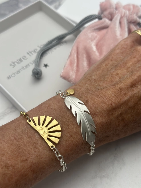 model wears a sterling silver feather charm on a silver belcher bracelet with mini heart charm in gold