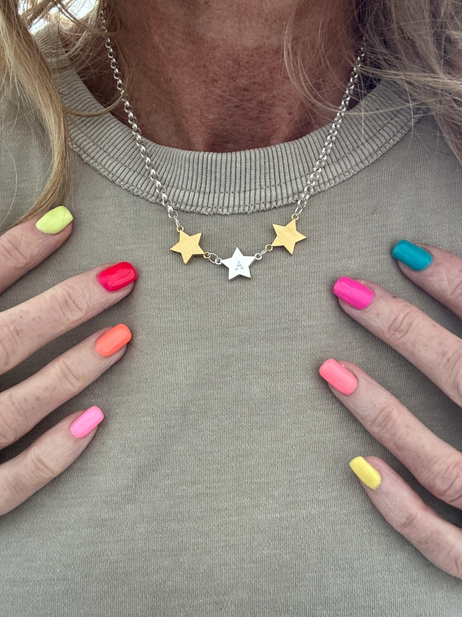 model wears a trio of linked star charms in mixed metal on a silver belcher chain