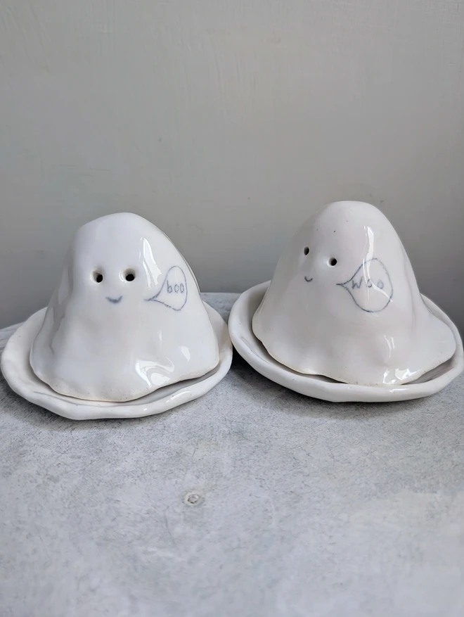 white ceramic Halloween ghost tealights in the shape of a tiny ghost with tiny cut out eye holes a smiley face and the word boo or woo in a speech bubble
