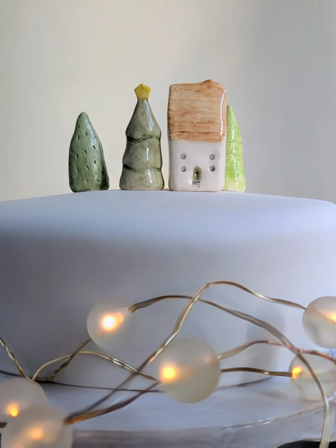 miniature ceramic house and tree cake topper ornament on a white Christmas cake