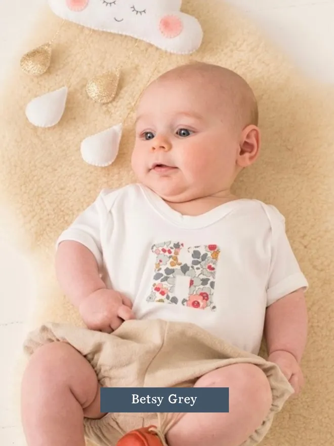  a new baby in a Liberty print initial baby bodysuit in a floral  Betsy Grey print