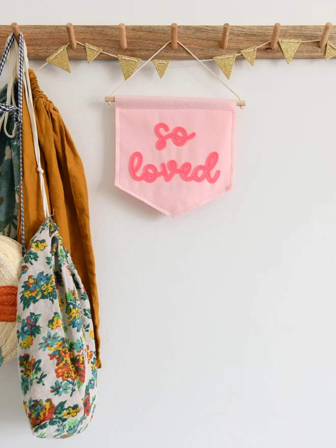 mini felt banner with so loved sewn on in pink cursive text.