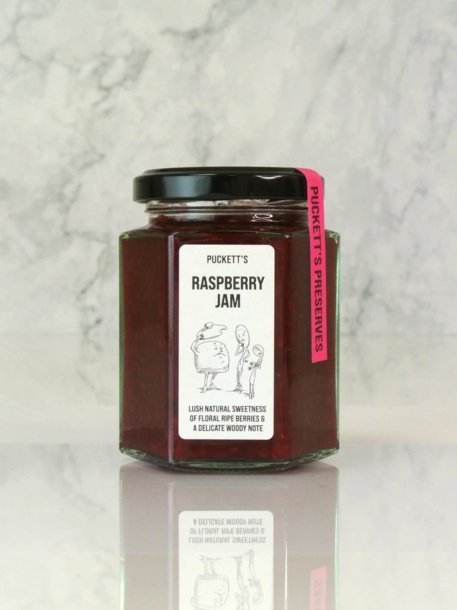 british raspberry jam. a jar of jam photographed against a marble background. 