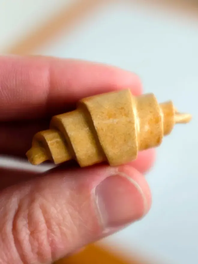 ceramic croissant hanging christmas decoration. a close up image of a small ceramic croissant.