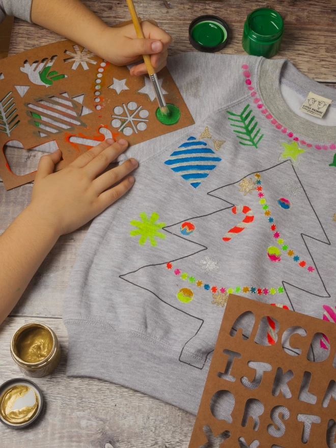 Hands stencilling onto a xmas tree printed sweat using fabric inks and stencils