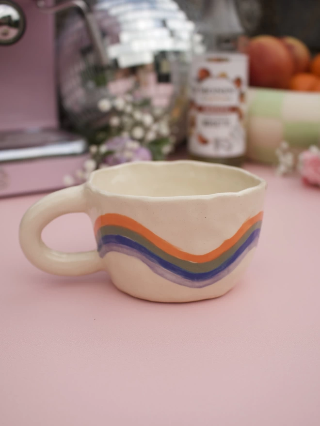 wavey stripes of orange, green, blue and purple around a handmade stoneware pottery mug