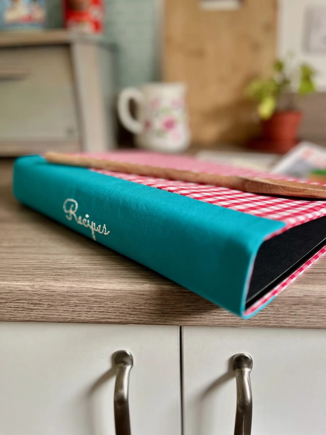 Ring binder with red and white gingham cover in kitchen. ‘Recipes’ embroidered on the teal spine
