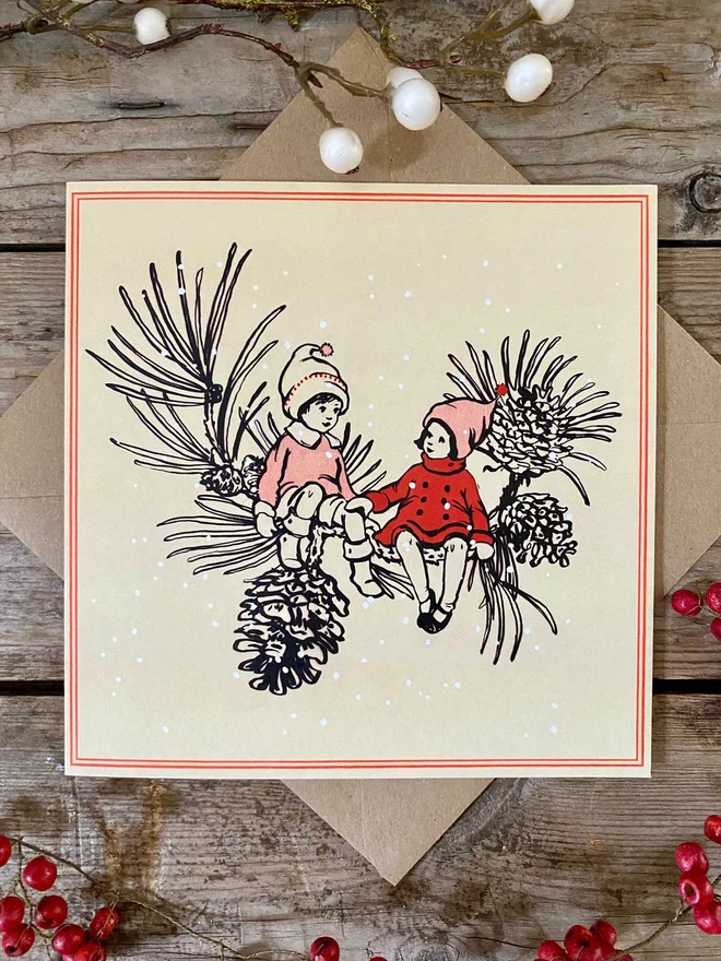 Christmas card featuring a storybook vintage style illustration of 2 pixies sat on a pine branch in the snow. card is yellow with a red border