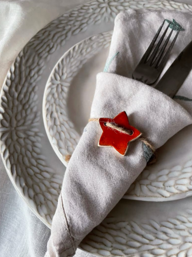 Ceramic Star Napkin Ring tied around some cutlery and a napkin on a ceramic plate