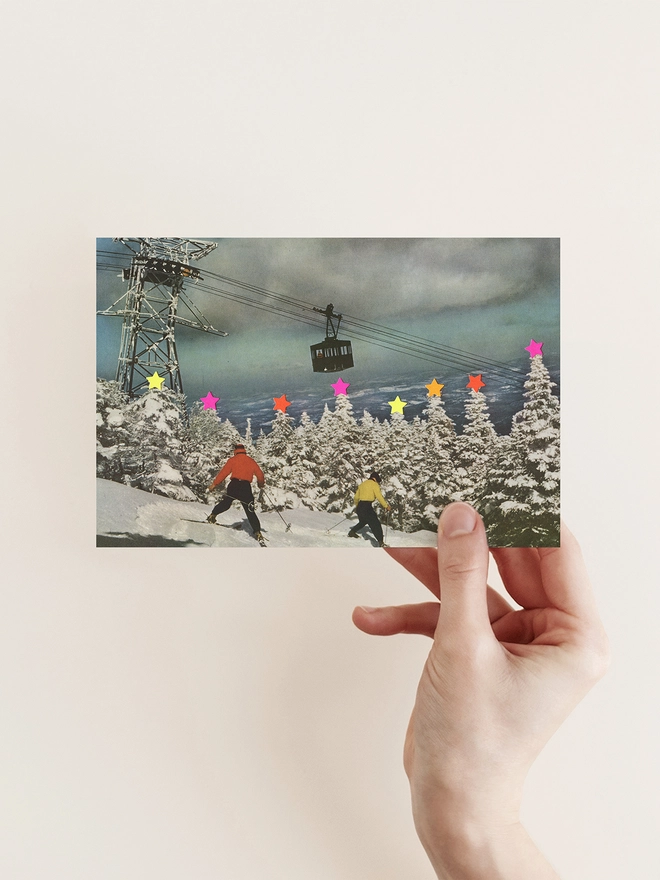 Two skiers are awkwardly sliding down a ski slope covered in snow. Thre are lots of snow covered trees with neon stars on top. 