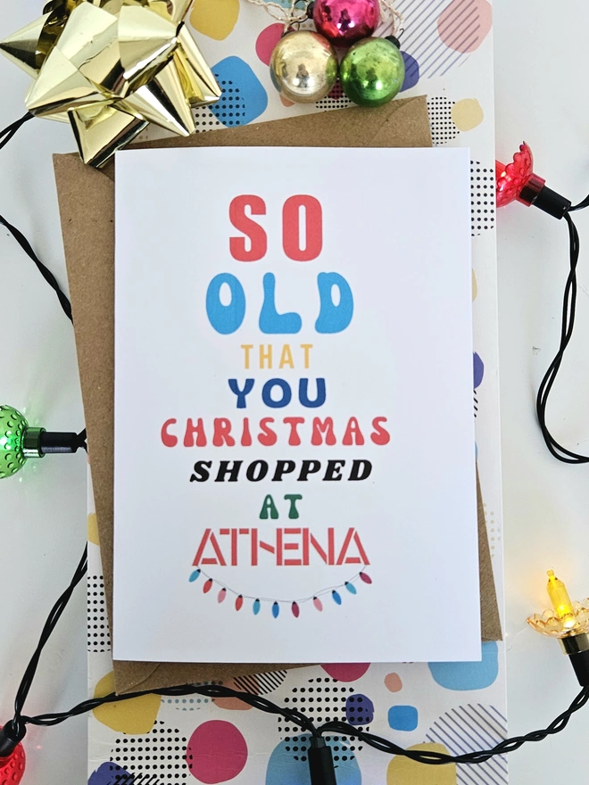 A photograph of the front of a humorous A6 greeting card illustrated using brightly coloured text and the retro shop logo. The text says so old you Christmas shopped at Athena