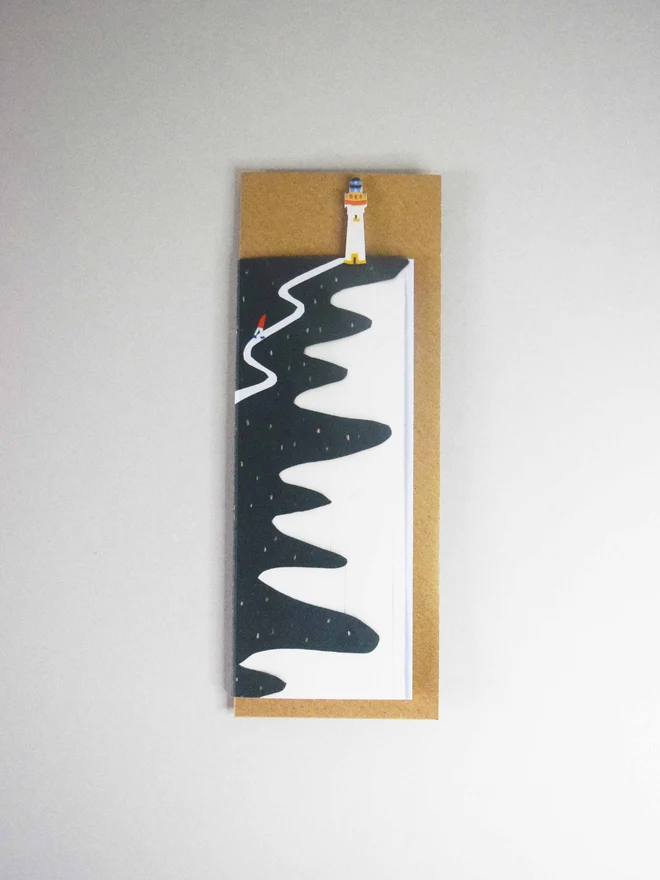 A cut out card of a cliff with a lighthouse on top of an envelope