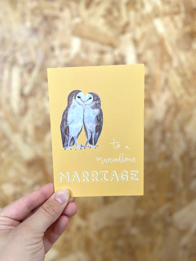 a greetings card with a bright yellow background featuring two kissing barn owls and the phrase ‘to a marvellous MARRIAGE”