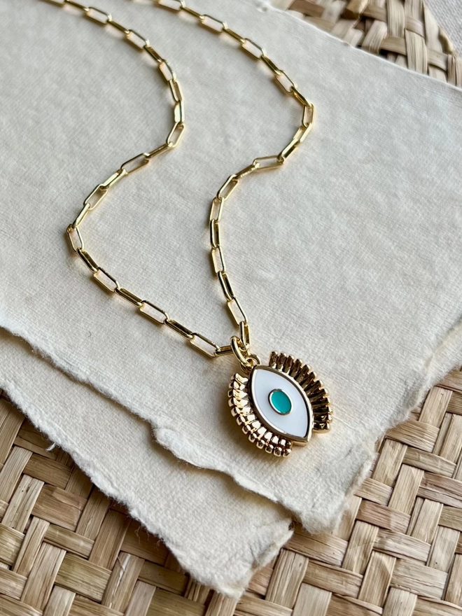 Turquoise and white enamel evil eye necklace on gold paperclip chain on a background of parchment paper
