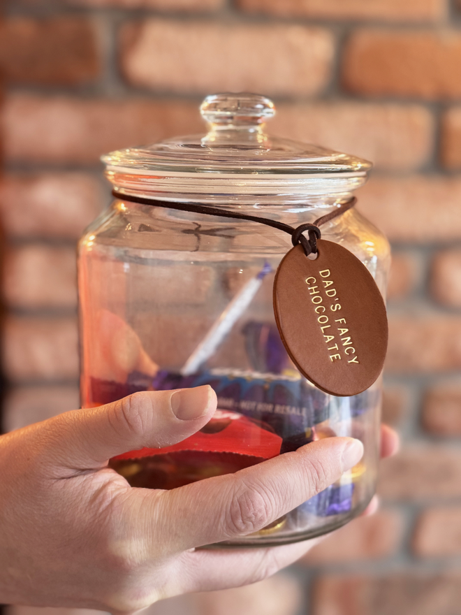 a glass jar with chocolate in, a leather label with 'Dad's Fancy Chocolate' stamped on the brown tag with gold writing.