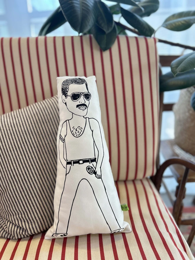 Black and white illustrated screen printed cushion of Queen frontman Freddie Mercury. The cushion sits on a striped sofa.