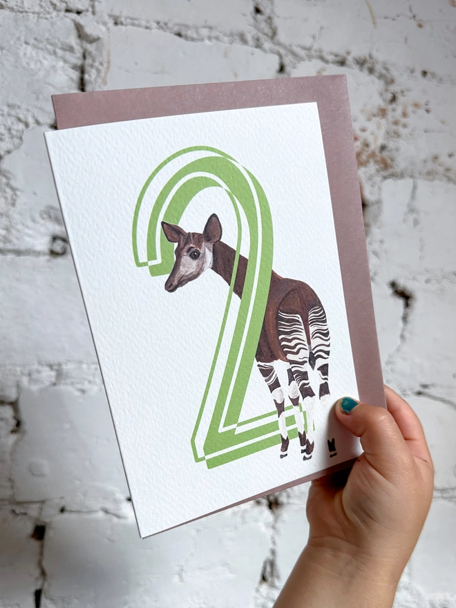 a white card with a big green number 2 and an illustration of an okapi with a purple envelope