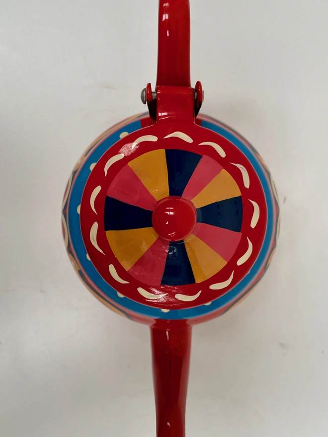 Lid of small red teapot, featuring a pink, yellow and blue striped design.