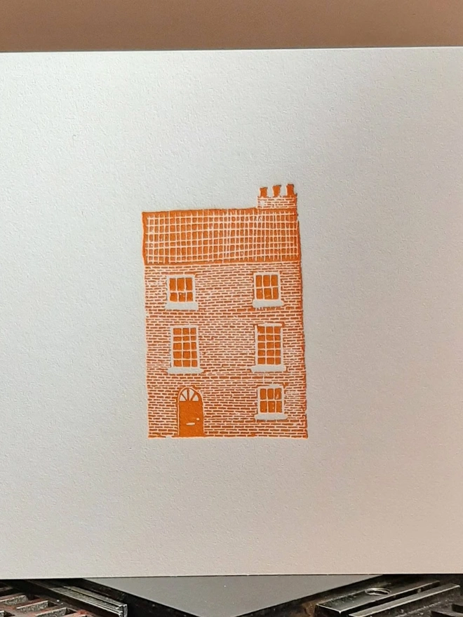 Orange Townhouse Letterpress Handprinted Greetings Card, a white card with an orange townhouse design in the centre. 