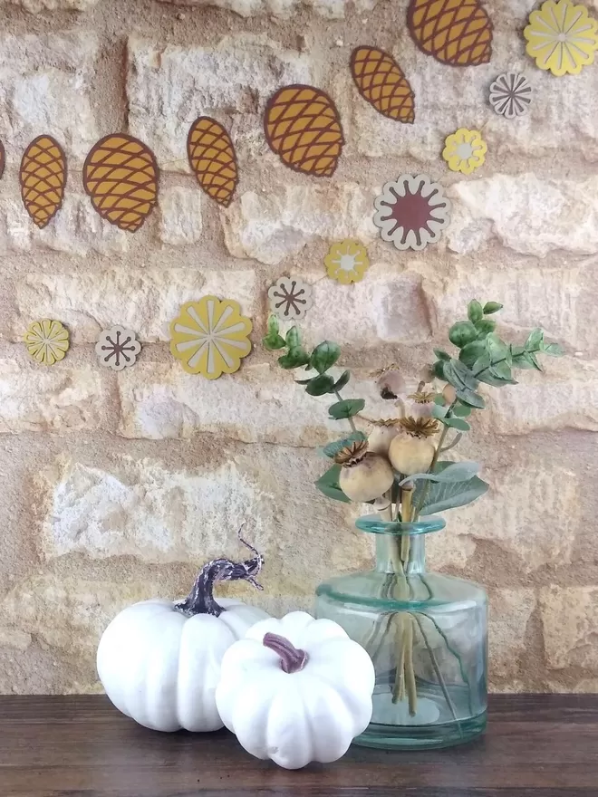 Pinecone Paper Garland displayed against stone wall with autumn foliage decorating the table below