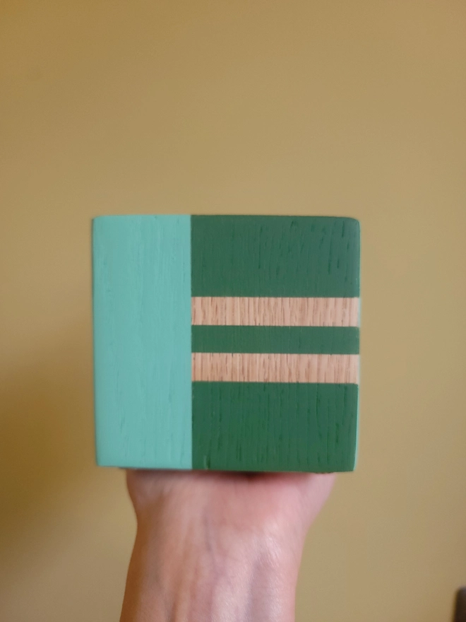 Wood cube tealight holder painted green and mint E held against yellow background