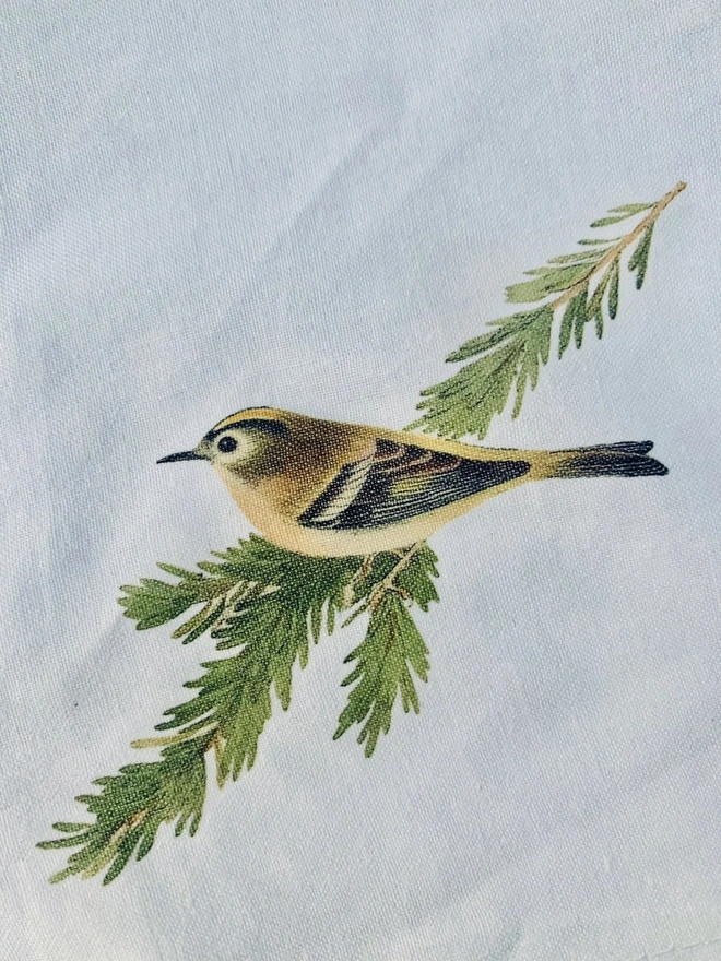 A white cotton napkin printed with a vintage illustration of a goldcrest