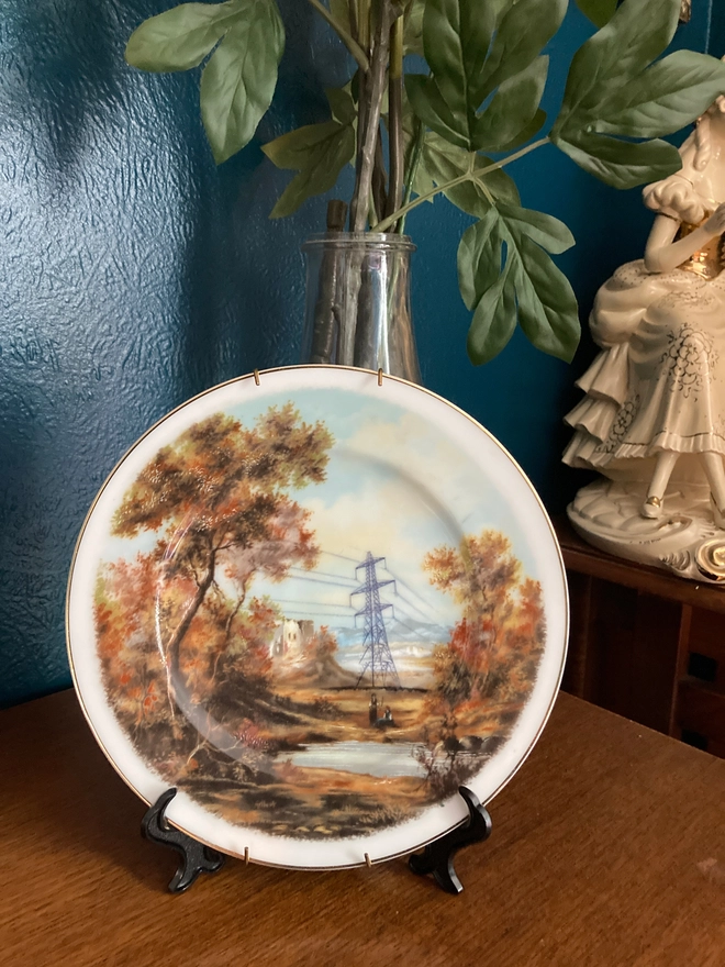 Vintage plate featuring an autumnal countryside scene with and a pylon in the center.